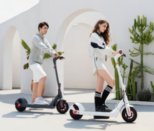 Man and woman riding Bremer R-Series electric scooters in an outdoor setting with modern architecture and plants.