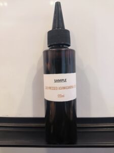 A 120ml bottle labeled 'SAMPLE COLD PRESSED ASHWAGANDHA OIL' from Rumali Supreme Company Ltd.