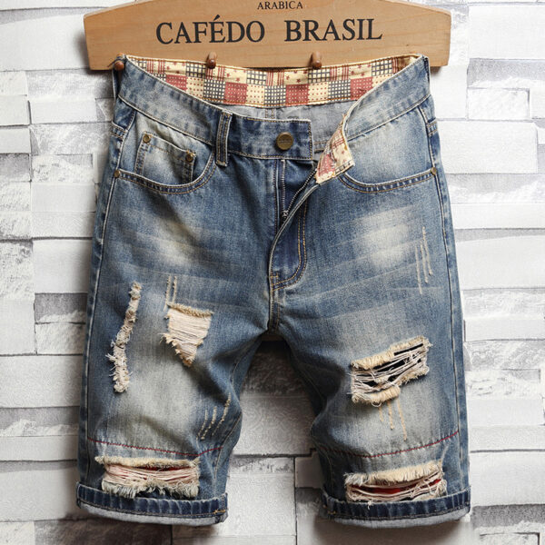 Distressed denim shorts with a patterned inner waistband displayed on a wooden hanger against a brick wall background.