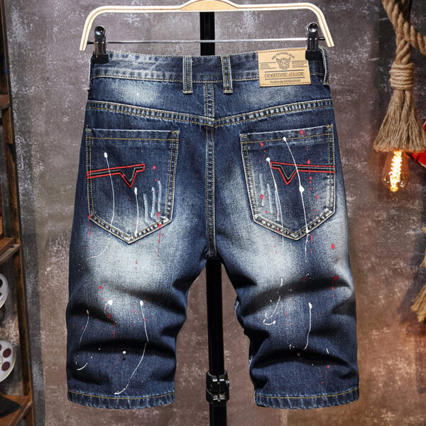 Designer distressed denim shorts with red stitching and paint splatter details, hanging on a rack.